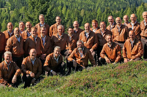 L'immagine mostra i componenti del coro in un prato all'aperto e sullo sfondo il monte Peller da cui il coro prende il nome